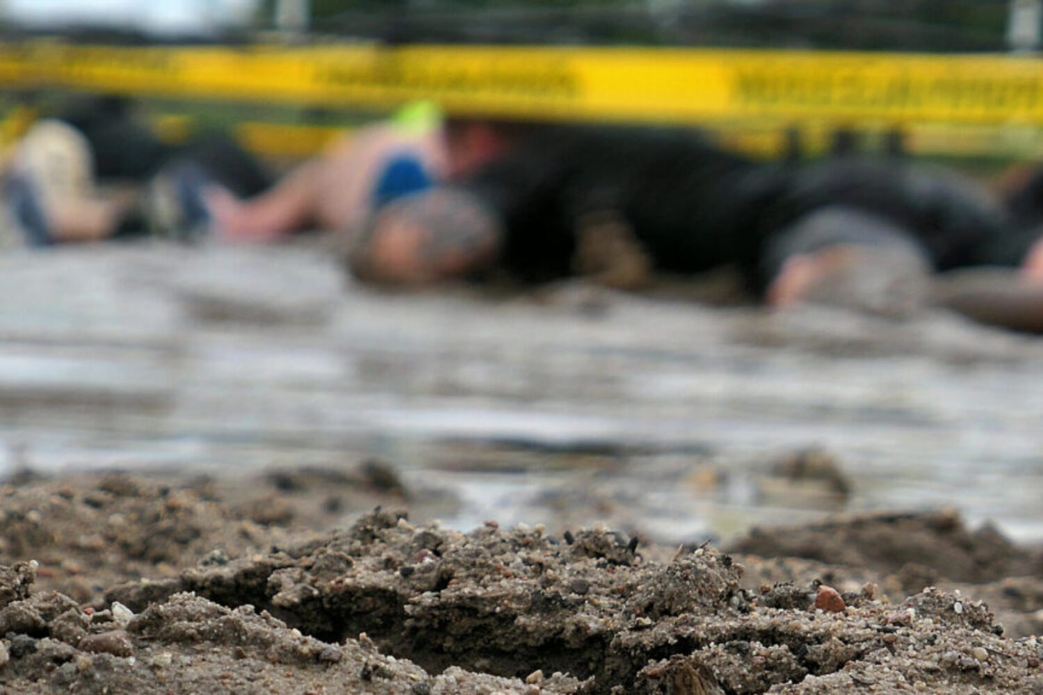 Competitors Crawling In Mud Under Barbed Wire In Obstacle Endurance Race